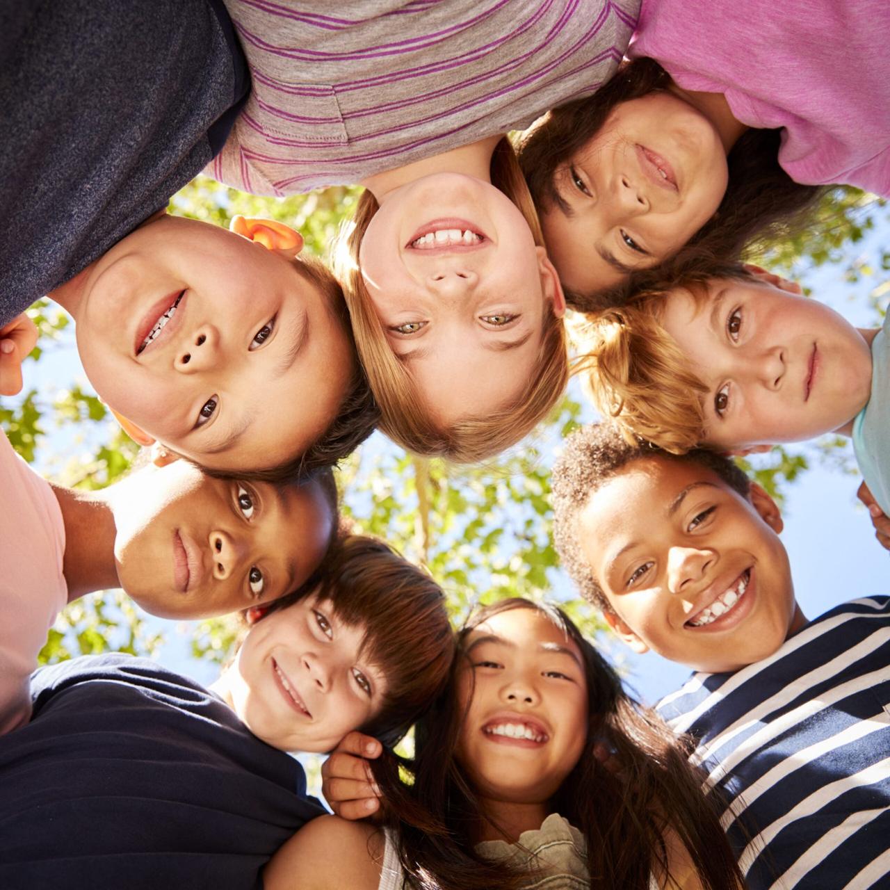 A circle of smiling children lying on the grass looking down at the camera