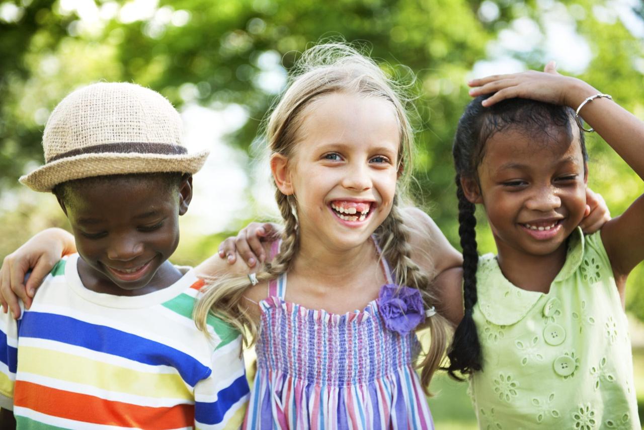 Four children in overalls and summer clothes smiling in a park